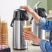 A woman using a Choice 2.2 Liter Glass Lined Stainless Steel Airpot to pour coffee into a cup.