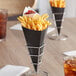 A black Carnival King cardboard fry cone filled with French fries on a table.