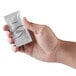A hand holding a small white and gray packet of Dial White Marble Breck Shampoo.
