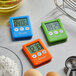 Four San Jamar digital kitchen timers in different colors on a white surface.