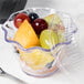 A clear plastic Cambro swirl bowl filled with fruit on a hospital cafeteria counter.