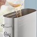 A person pouring brown liquid into a stainless steel Choice 4 Gallon Iced Tea Dispenser.