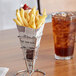 Carnival King News Print Square Cardboard Fry Cone filled with French fries on a table next to a glass of ice tea.