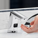 A person's hand pressing a Sloan polished chrome sensor soap dispenser above a sink.