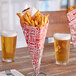 A Carnival King square cardboard fry cone filled with french fries on a table with two glasses of beer.