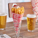 A Carnival King cardboard fry cone filled with French fries in a container on a table with a glass of beer.