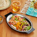 A Choice oval stainless steel sizzler platter with shrimp, vegetables, and tortillas on it.