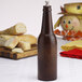 A brown bottle on a table next to bread.