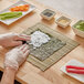 A person wearing gloves rolls sushi on a table using an Emperor's Select bamboo sushi mat.