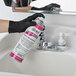 A person in black gloves using a Noble Chemical spray can to clean a bathroom sink.