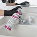 A person in black gloves using Noble Chemical Scum-B-Gone aerosol spray to clean a bathroom sink.