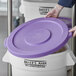 A person wearing gloves putting a purple Baker's Mark lid on a white container.