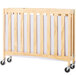 A natural wood slatted folding crib with wheels.