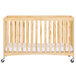 A natural wood full size folding crib with wheels.