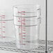 Three Cambro clear round food storage containers on a metal shelf.