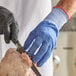 A person wearing Mercer Culinary blue cut-resistant gloves cutting meat with a knife.