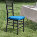 A Lancaster Table & Seating Black Wood Chiavari Chair with a blue cushion on a table with a white tablecloth in the grass.