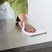 A person cleaning a stainless steel counter with a ChoiceHD white foodservice wiper.