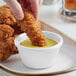 A person dipping a fried chicken strip into a white Acopa fluted ramekin of sauce.