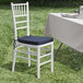A Lancaster Table & Seating white wood Chiavari chair with a navy blue cushion on it next to a table.