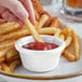 A hand dipping a french fry into a white Acopa fluted ramekin.