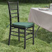 A Lancaster Table & Seating black wood Chiavari chair with a green cushion on a table outdoors.