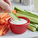 A hand dipping a carrot into a red Acopa fluted ramekin of dip.