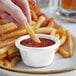 A hand holding a french fry being dipped into a white Acopa ramekin of ketchup.