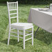 A Lancaster Table & Seating white Chiavari chair with an ivory cushion sits next to a table.
