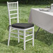 A Lancaster Table & Seating white wood Chiavari chair with a black cushion next to a table.
