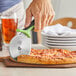 A person using a Mercer Culinary pizza cutter with a green handle to cut a pizza.