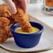 A person dipping a fried chicken strip into a blue Acopa fluted melamine ramekin of sauce.
