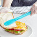 A person using a Choice neon blue sandwich spreader to spread butter on a sandwich.