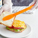 A person using a Choice neon orange sandwich spreader to cut a sandwich.