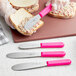 A person spreading food on a piece of bread with a Choice stainless steel sandwich spreader with a neon pink handle.