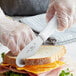 A person cutting a sandwich with a Choice scalloped sandwich spreader.