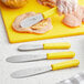 A stainless steel sandwich spreader with a yellow handle being used to cut chicken.