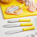 A white scalloped sandwich spreader with a yellow handle being used to cut chicken.