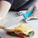 A person using a Choice scalloped sandwich spreader to spread butter on a sandwich.