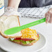 A person using a Choice neon green sandwich spreader to spread on a sandwich.