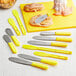A Choice stainless steel sandwich spreader with a yellow handle on a counter.