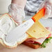 A person using a Choice sandwich spreader with a neon orange handle to spread butter on a sandwich.