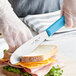 A person cutting a sandwich with a Choice scalloped sandwich spreader.