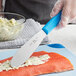 A person's hand with a Choice blue scalloped sandwich spreader cutting a piece of fish.