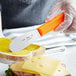 A person using a Choice stainless steel sandwich spreader with a neon orange handle to spread butter on a piece of bread.