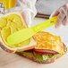 A gloved hand uses a Choice yellow polypropylene sandwich spreader to spread butter on a sandwich.