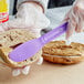 A person using a Choice purple polypropylene sandwich spreader to spread peanut butter on a bagel.