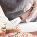 A person holding a Choice stainless steel sandwich spreader and spreading food on a piece of bread.