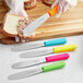 A Choice stainless steel sandwich spreader with a neon orange handle spreading food on a piece of bread.