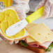 A Choice sandwich spreader with a yellow handle cutting a sandwich.